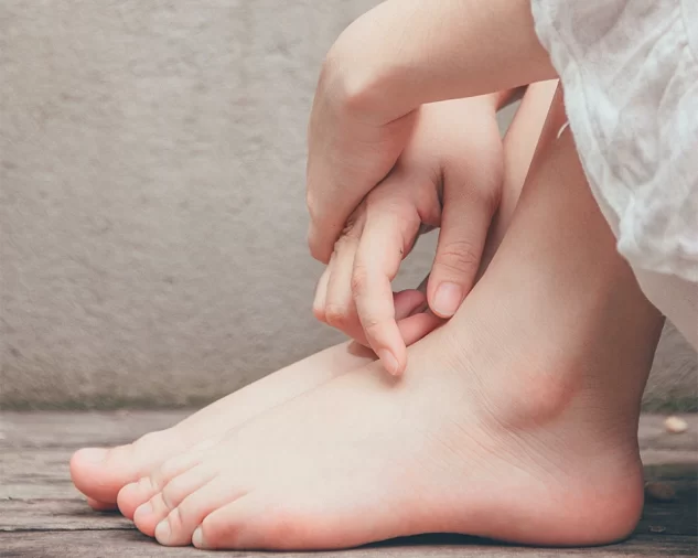 A person seated on a rustic wood floor, close up of their hands folded over their bare feet.